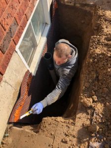 man in excavated hole installing a window well drain