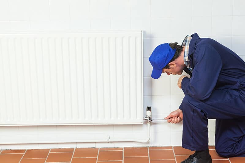 plumber installing radiator into tiled wall